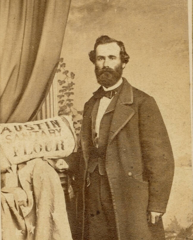 Black and white cartes de visite photograph of a man in a long dark jacket next to a sack of sanitary flour.